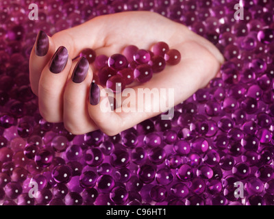 Lizenz erhältlich bei MaximImages.com Frauenhand mit violettem nagellack auf abstraktem rosa Süßwarenhintergrund Stockfoto