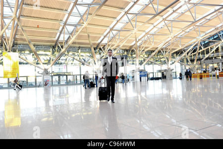 Junge, selbstbewusste Geschäftsmann, Reise trägt einen Anzug und Wandern mit Gepäck für ein Unternehmen am Flughafen, Hamburg, Deutschland Stockfoto