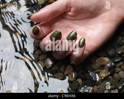 Lizenz erhältlich unter MaximImages.com Nahaufnahme der Frauenhand mit grünem, feinem nagellack im Wasser Stockfoto
