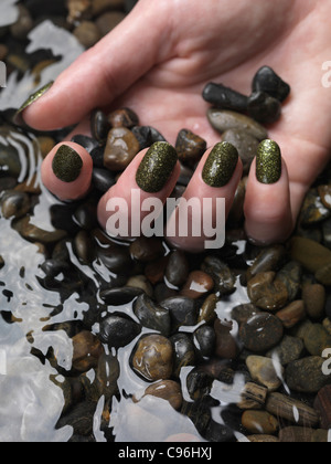 Lizenz erhältlich unter MaximImages.com Großaufnahme der Frauenhand mit grünem, feinem nagellack, der im Wasser auf Kieselsteinen liegt Stockfoto