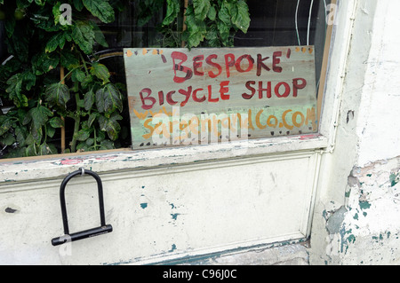 Schild mit der Aufschrift "maßgeschneiderte" Fahrradgeschäft in Ecke der Schaufenster mit Schloss Sie an Wand außen, Sargent und co, Hackney Stockfoto