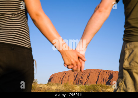 Paar Hand in Hand mit Uluru (Ayers Rock) im Hintergrund.  Uluru-Kata Tjuta National Park, Northern Territory, Australien Stockfoto