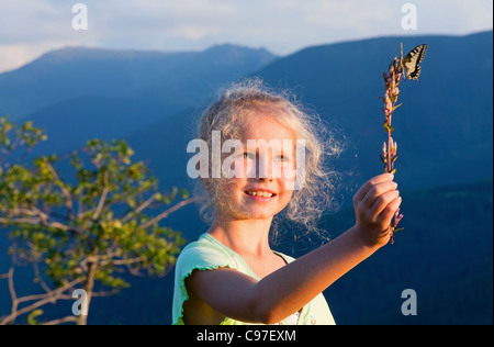 Kleines Mädchen im Sonnenuntergang Berg bewundern auf gelbe Schwalbenschwanz-Schmetterling Stockfoto