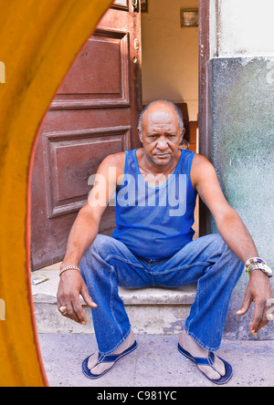 Kubanische Mann, mit einem sehr unglücklichen Blick auf seinem Gesicht sitzt auf den Schritt der Eingangstür seines Hauses in Havanna, Kuba. Stockfoto