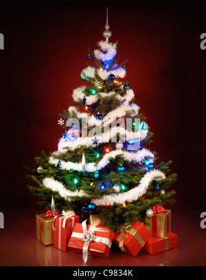 Scheint dekorierten Weihnachtsbaum mit Geschenken unter ihm. Isoliert auf dunkelroten Hintergrund. Stockfoto