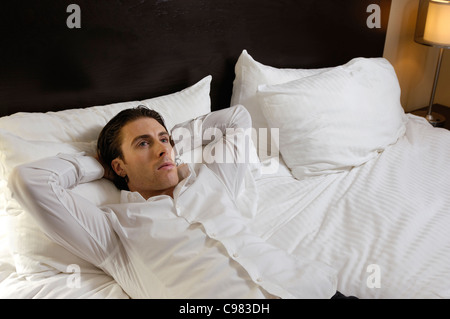 Junger Mann liegt allein im Bett mit nachdenklichen Ausdruck Stockfoto