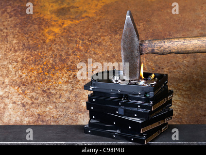 symbolische Daten Zerstörung Thema zeigt die Details eines Hammers auf ein Stapel brennen Festplatten vor rostigen zurück Stockfoto