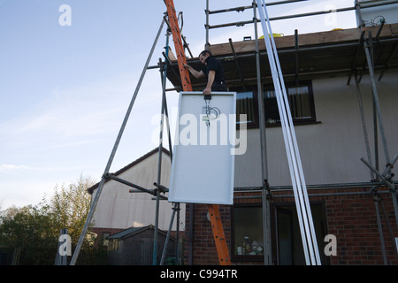 UK Jüngling heben ein Solar-Panel, ein Aufstieg von Gerüsten auf heimischen Hausdach passen Stockfoto