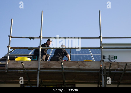 UK zwei Männer stehen auf einem Gerüst Montage Sonnenkollektoren auf einem inländischen Hausdach unter Futter im Tarif FIT System Stockfoto