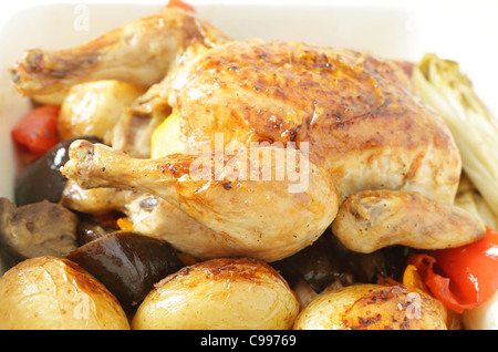 Gebratenes Huhn in einer Schüssel auf einem Bett von Ofen gebraten Gemüse einschließlich Kartoffeln, Paprika, Chicorée, Auberginen und Knoblauch. Stockfoto