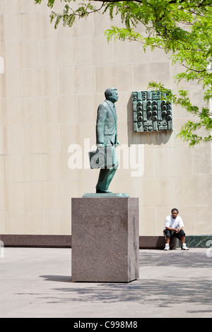 Schwarzer Mann sitzt, Blick auf die Statue des James A. Rhodes vor der State Office Tower in der Innenstadt von Columbus, Ohio. Stockfoto