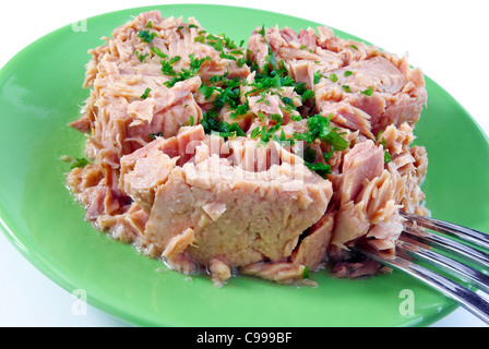 Dose Thunfisch mit etwas Petersilie auf einer grünen Platte isoliert auf weiss Stockfoto