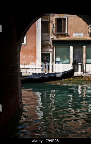 Zeigen Sie in Venedig durch einen Torbogen vom Ende einer Gondel und einer Frau zu Fuß, mit Reflexionen in den Kanal erblickt an. Stockfoto