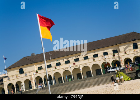 Rote und gelbe Surf Lifesaving Flagge mit dem Bondi Pavilion im Hintergrund. Bondi Beach, Sydney, New South Wales, Australien Stockfoto