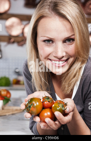 Italien, Toskana, Magliano, Nahaufnahme, junge Frau mit Tomaten in Küche, Lächeln, Porträt Stockfoto