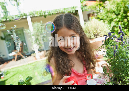 Deutschland, Bayern, Mädchen bläst Seifenblasen im Garten, Lächeln, Porträt Stockfoto