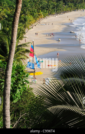 Mexiko, Guerrero, Zihuatanejo, Blick auf Playa la Ropa Strand mit Menschen auf der Kokospalme, von Bäumen gesäumten Strand Stockfoto