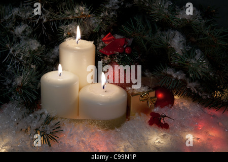 Weihnachts-Geschenk-Boxen mit brennen Kerzen unter geschmückten Tanne auf Schnee Stockfoto