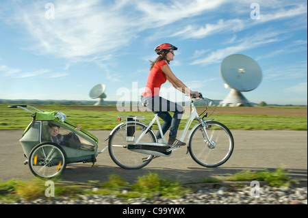 Deutschland, Bayern, Raisting, Frau mit Mädchen reiten Kinderanhänger in der Nähe von Radiosender Stockfoto