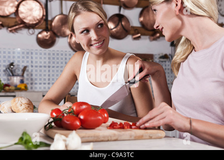 Italien, Toskana, Magliano, zwei junge Frauen schneiden Tomaten in Küche, Lächeln Stockfoto