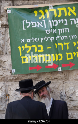 Zwei orthodoxe Juden mit Plakat auf Hebräisch in bkgd. Mea Shearim Nachbarschaft zu reden. Jerusalem Stockfoto