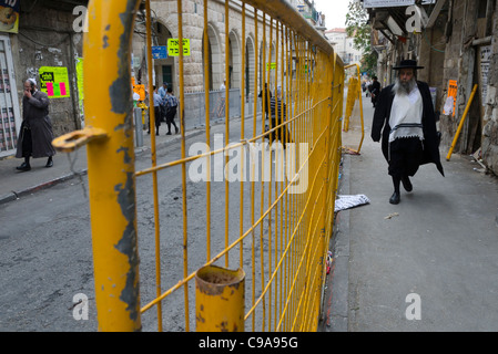 Orthodoxe Juden, die zu Fuß in einer Straße mit einem Zaun. Mea Shearim. Jerusalem. Israel. Stockfoto