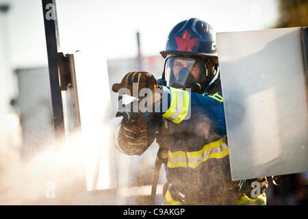 Ein Feuerwehrmann aus Kanada soll ein Feuerwehrschlauch auf ein Ziel beim vollen Brandbekämpfung Ausrüstung tragen und arbeiten gegen die Zeit während das internationale Finale des Firefighter Combat Challenge am 18. November 2011 in Myrtle Beach, South Carolina. Stockfoto