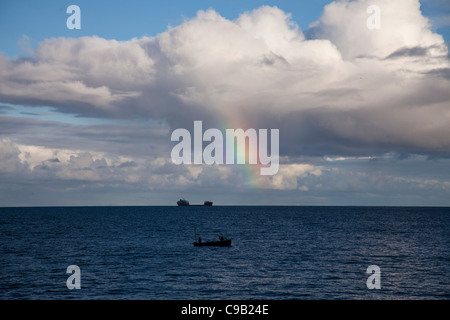 Fischer Fische im Meer off nur die Eidechse in Cornwall, UK, vor einem Frachtschiff am Horizont Stockfoto