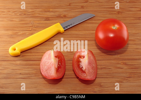 Tomate, Messer und zwei Tomaten Vierteln auf ein Schneidebrett Stockfoto