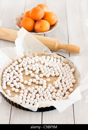 Eine Aprikose Torte machen: Teig gerollt, Konserve Torte mit Gewichten fertig zum Backen. Nudelholz und Aprikosen auf Holztisch Stockfoto