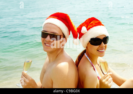 Porträt von attraktives Paar in Santa Mützen und Sonnenbrillen Blick in die Kamera am Strand Stockfoto