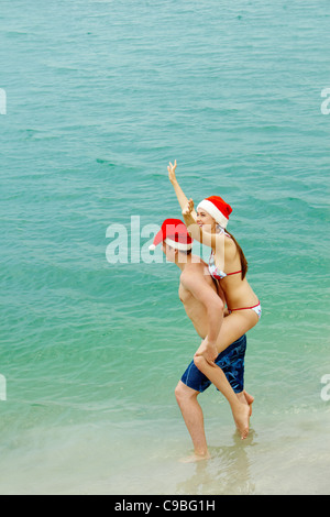 Porträt von glücklicher Mann und Frau in Santa Caps Spaß im Wasser Stockfoto