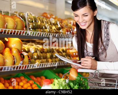 Bild hübsche Frau Wahl Produkte im Supermarkt mit Liste der Dinge zu kaufen Stockfoto