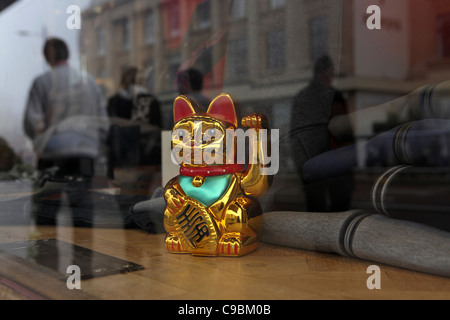 Goldenen chinesischen Glück Geld Katze, Wellen an Passanten durch Fenster der Herren Kleidung Shop, Norwich, Norfolk, Großbritannien Stockfoto