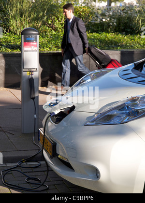 Elektroauto Nissan Leaf angeschlossen und geladen in Amsterdam, die Niederlande mit Mann vorbeigehen Stockfoto