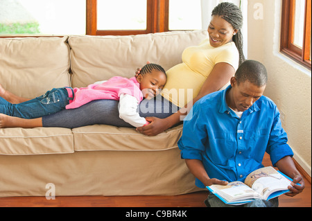 Mädchen auf schwangeren Bauch liegend, während ihr Vater Ihnen, Johannesburg, Provinz Gauteng, Südafrika liest Stockfoto