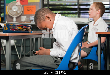 Junge mit Mobiltelefon unter Schreibtisch im Klassenzimmer, Johannesburg, Provinz Gauteng, Südafrika Stockfoto