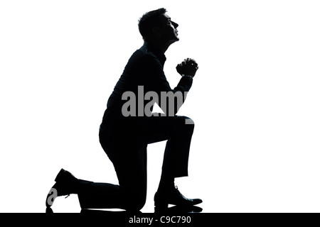 ein kaukasischer Mann kniend beten in voller Länge-Silhouette im Studio isoliert weißen Hintergrund Stockfoto