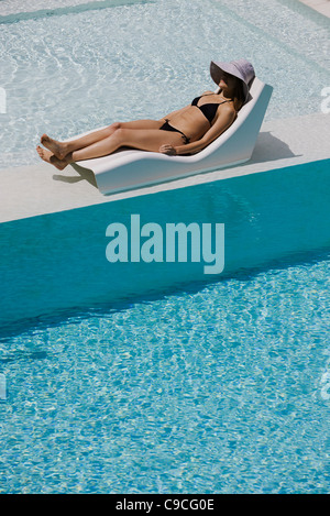 Junge Frau trägt Sonne Hut liegen im Liegestuhl am Pool Stockfoto