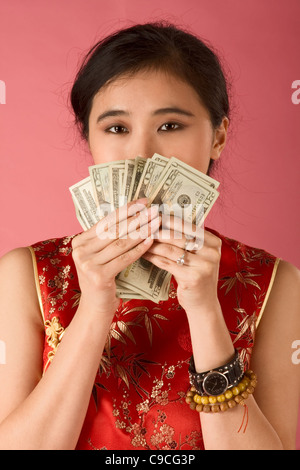 Porträt der jungen Chinesin in traditioneller Kleidung (Cheongsam) mit zwanzig Dollar Bills, bedeckte ihr Gesicht von ihnen. Stockfoto