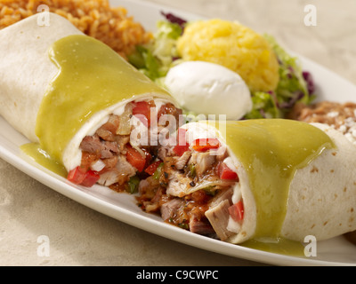 Carnitas Burrito mit Tomatillo Salsa und Sauerrahm garniert und serviert mit gebackenen Bohnen und Reis Spanisch Stockfoto