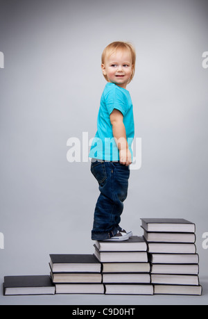 Kleiner Junge zu Fuß auf den Führer der Bücher Haufen gemacht Stockfoto