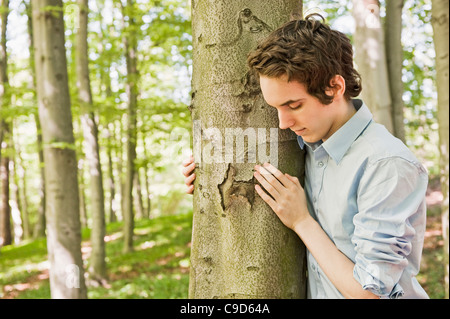 Junge Mann stand durch einen Baum im Wald Stockfoto
