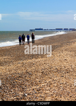 Vier Menschen zu Fuß auf einem Strand nördlich von Southwold an der Küste von Suffolk im östlichen England UK mit dem Pier in der Ferne Stockfoto