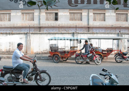 Ein Tuktuk-Fahrer parkt vor dem Gelände der ehemaligen High School, die von den Roten Khmer als berüchtigtes Sicherheitsgefängnis 21 (S-21) genutzt wurde. Am 4. Februar 2012 verhängte die Berufungskammer der Außerordentlichen Kammern in den Gerichten Kambodschas eine lebenslange Haftstrafe Stockfoto