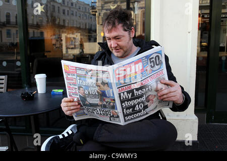 Ein Mann im Bild, lesen die neue Sonne am Sonntagszeitung vor einem Geschäft in Brighton, East Sussex, UK. Stockfoto