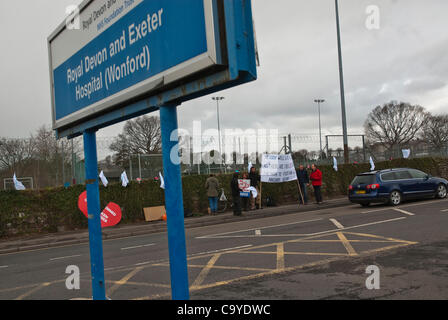 03.07.2012, Exeter, UK. Der königliche Devon & Exeter Eingang Schild mit einem Demontrating Actisists und Zeichen im Hintergrund, während der NHS-Reform-Protest vor dem Royal Devon & Exeter Krankenhaus. Stockfoto