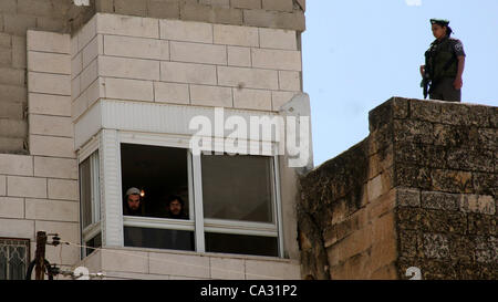 29. März 2012 - Hebron, Westjordanland, Palästinensische Autonomiegebiete - ein israelischer Siedler aus dem Fenster eines besetzten palästinensischen Hauses aussieht, wie ein israelischer Soldat Wache im Zentrum von Hebron im besetzten Westjordanland am 29. März 2012 steht. Dutzende von jüdischen Siedlern übernahm die palästinensischen Eigenschaft ov Stockfoto