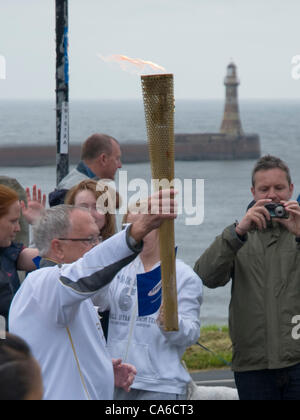 Fackelträger trägt das Olympische Feuer vorbei Roker Leuchtturm, während es Sunderland am Morgen des 16. Juni 2012 durchläuft Stockfoto