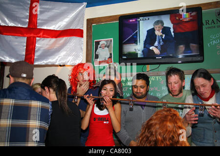 LA PAZ, BOLIVIEN, 24. Juni 2012. Eine Mischung aus englischen Reisenden und Expats, die während des Viertelfinalspiels der UEFA-Fußball-Europameisterschaft zwischen England und Italien (das live im Fernsehen dahinter übertragen wird) Trinkspiele spielen, in Olivers English Pub in La Paz. England-Manager Roy Hodgson ist mit einem besorgten Ausdruck auf dem Fernsehbildschirm im Hintergrund Stockfoto